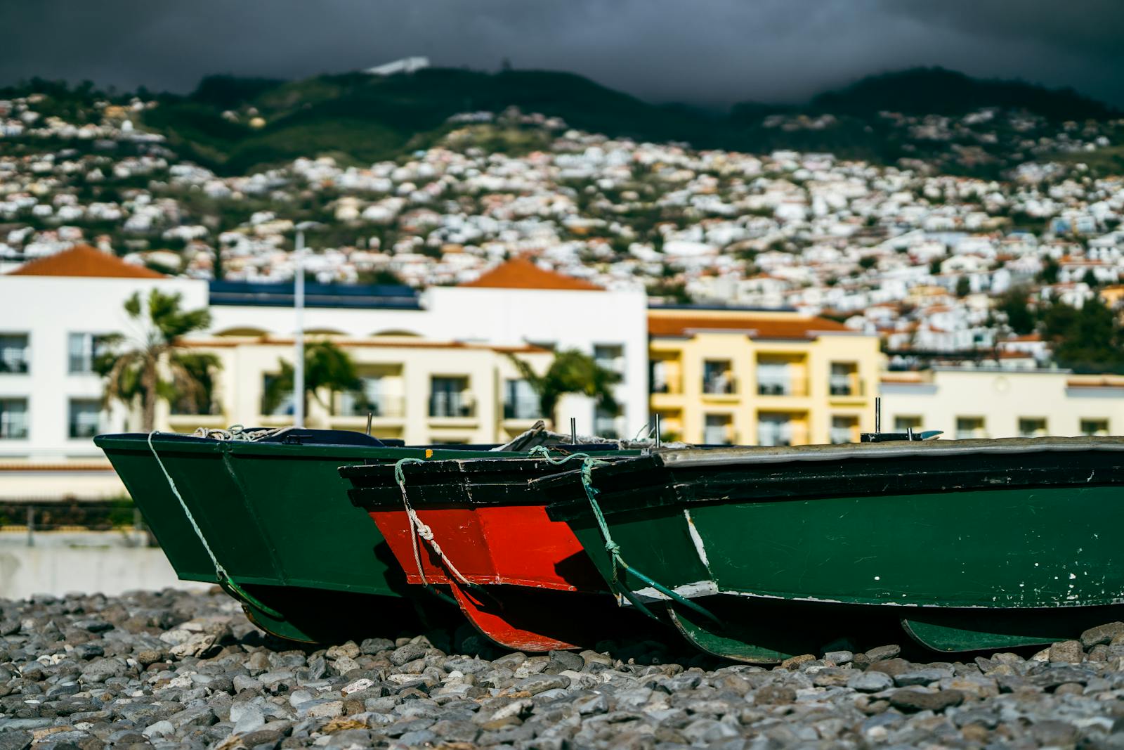 Vibrant fishing boats rest on the rocky shores of Madera with a coastal townscape in the background.