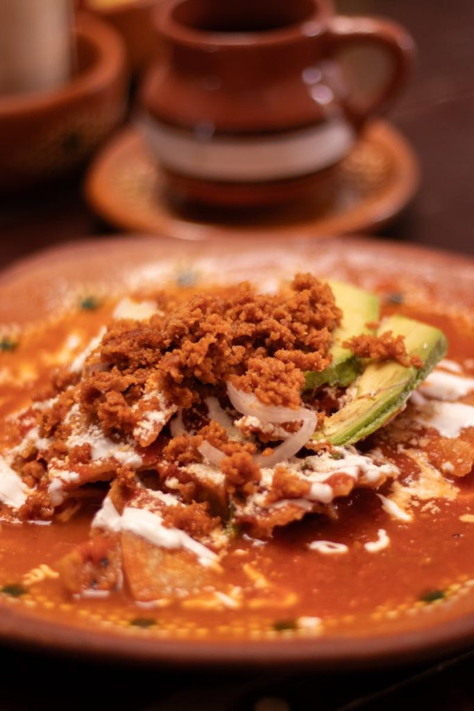 Traditional Mexican chilaquiles garnished with avocado and chorizo served on a clay plate.